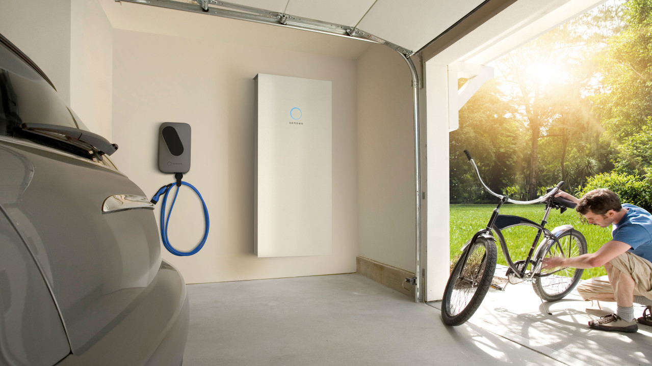 sonnenCharger next to the sonnenBatterie in a Garage, a man in front of the garage fixing his bike