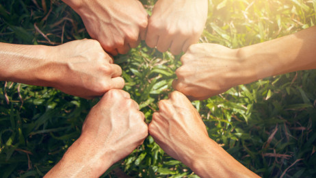 Six clenched fists join in a circle, symbolizing unity, solidarity, and teamwork