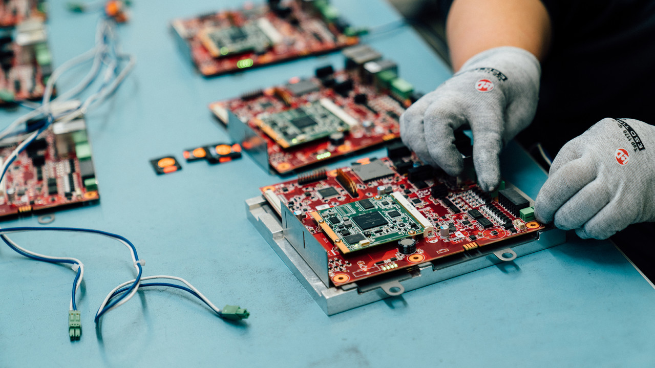 Leiterplatten der technischen Bestandteile der sonnenBatterie werden von einem Mitarbeiter mit Handschuhen zusammengesetzt.