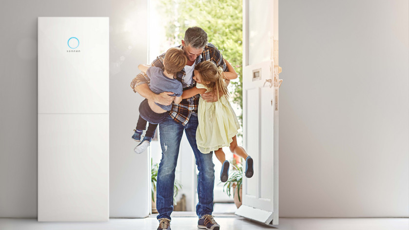 Far byder sine børn velkommen ved døren ved siden af en sonnenBatterie 