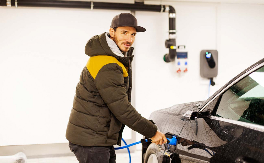 Felix Neureuther steht mit dem sonnenCharger an seinem Auto in seiner Garage