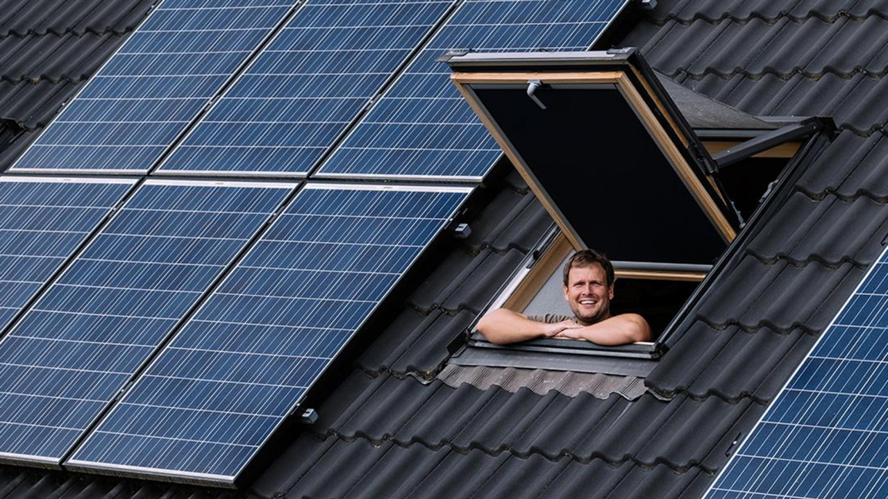 Botschafter Thomas Lutz schaut aus seinem Dachflächenfenster, neben dem Fenster sieht man PV-Module auf seinem Dach.