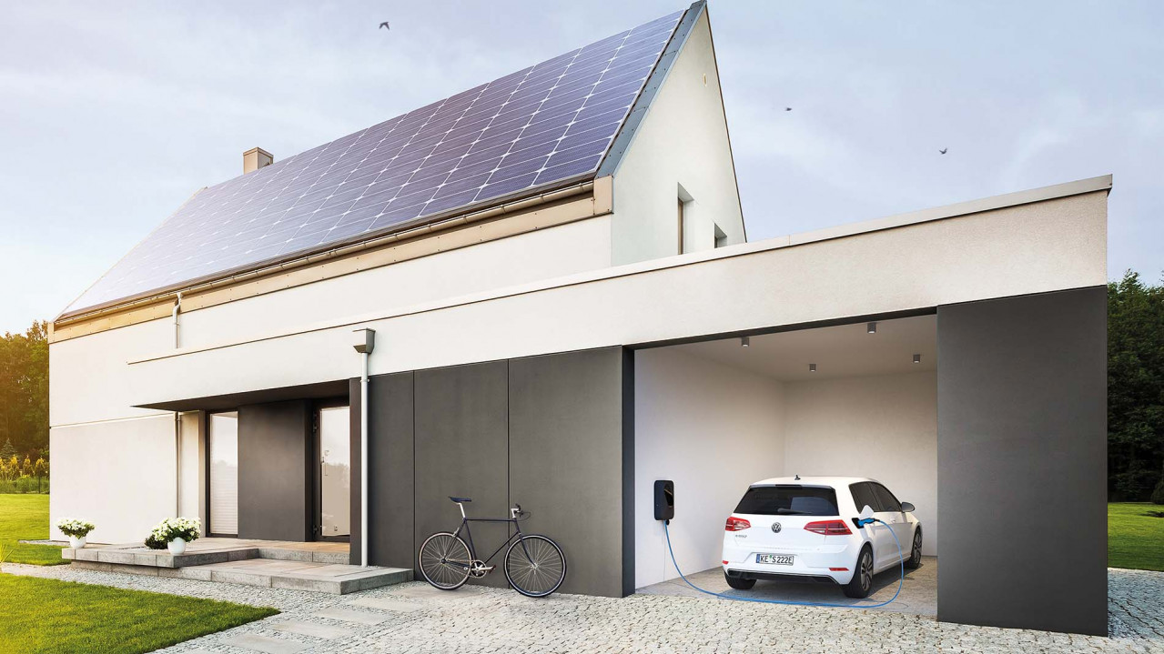 Ein Elektroauto steht in einer Garage neben einem Haus mit PV Modulen und wird mit einem sonnenCharger mit Strom geladen.
