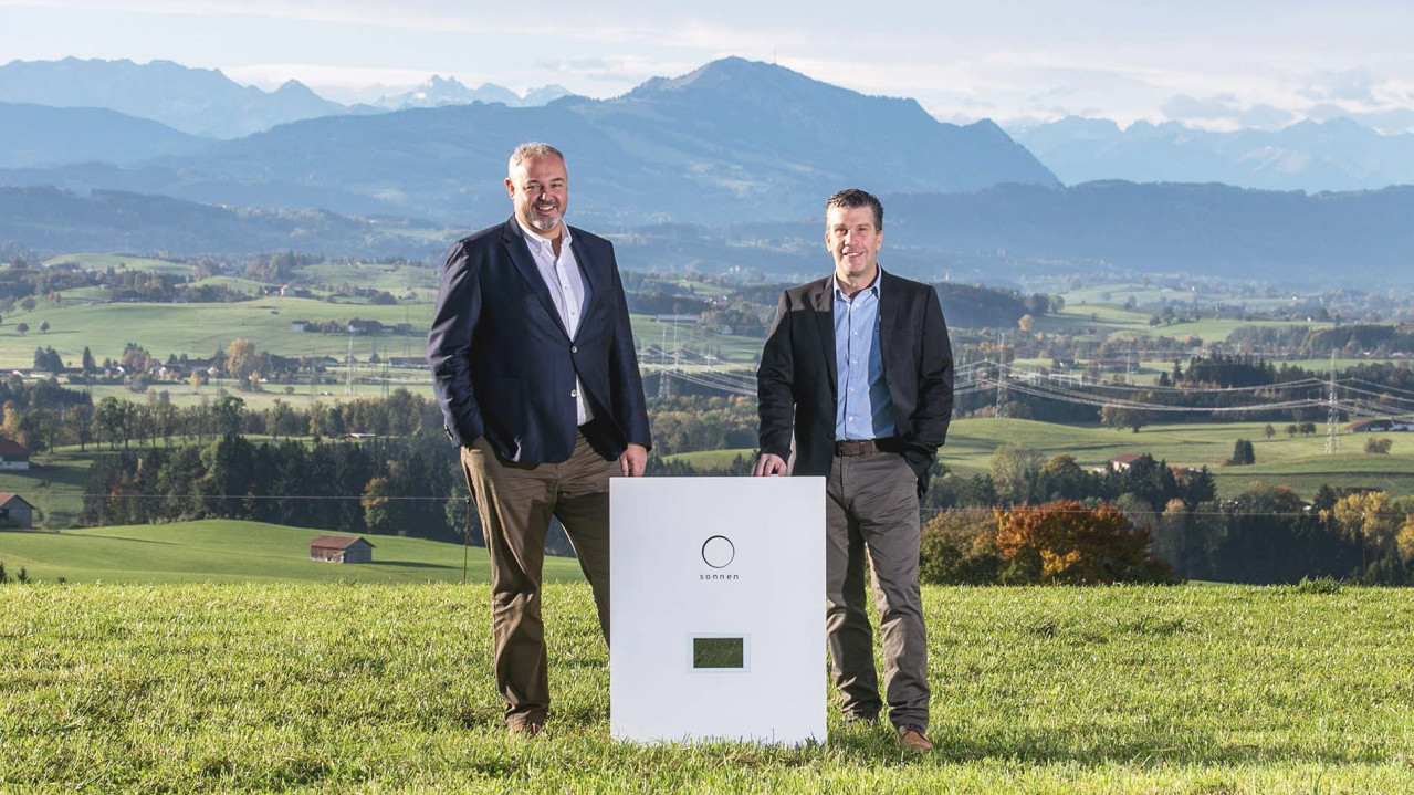 Christoph Ostermann und Torsten Stiefenhofer stehen zusammen mit einer sonnenBatterie im Allgäu auf einer Wiese.