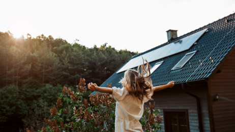 Chica feliz delante de su casa verde.