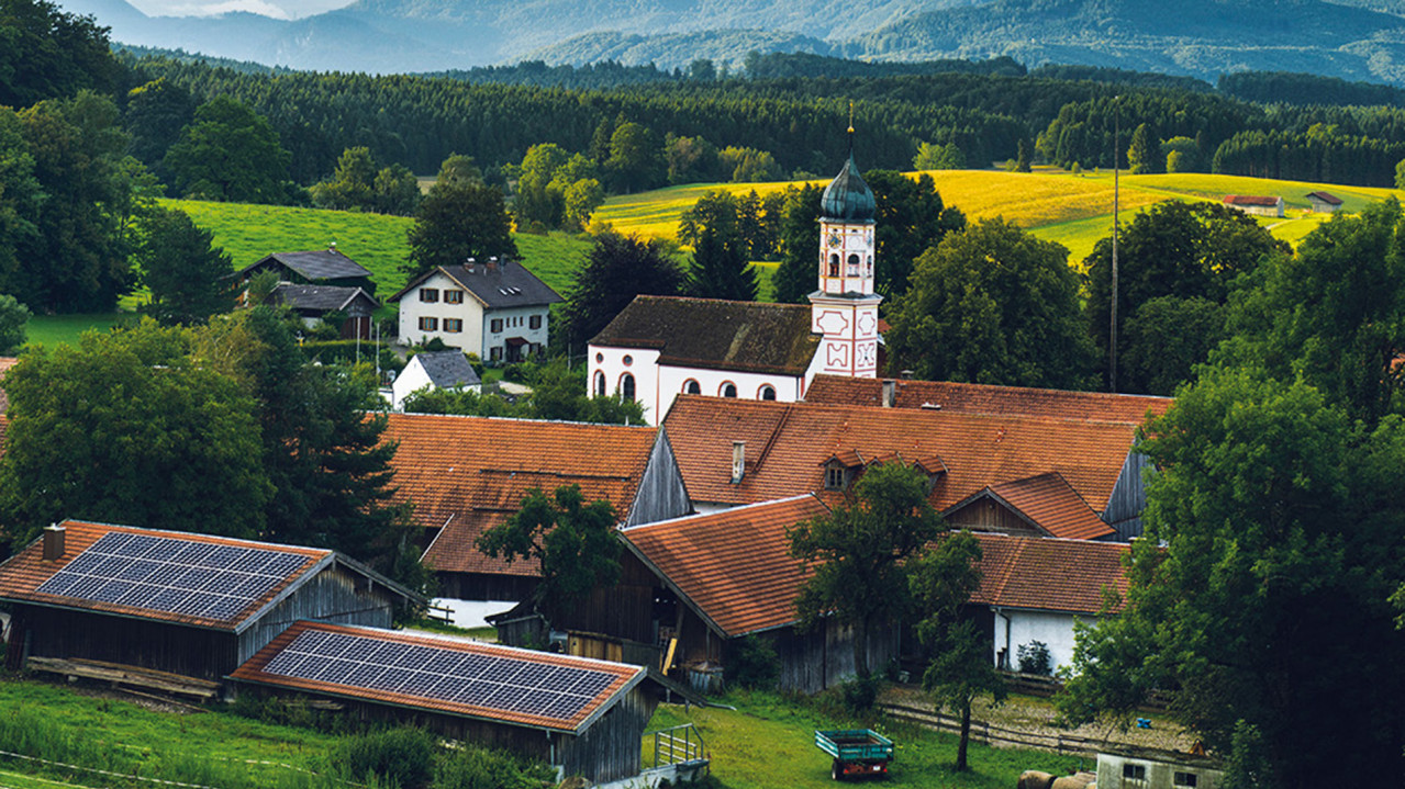 Ein kleines Dorf mit einer Kirche und einigen Häusern mit PV-Anlagen.