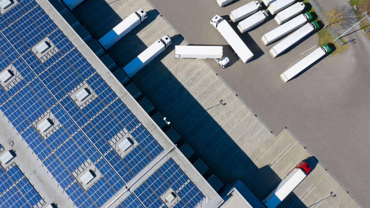 Una empresa con camiones y paneles fotovoltaicos en el tejado. 